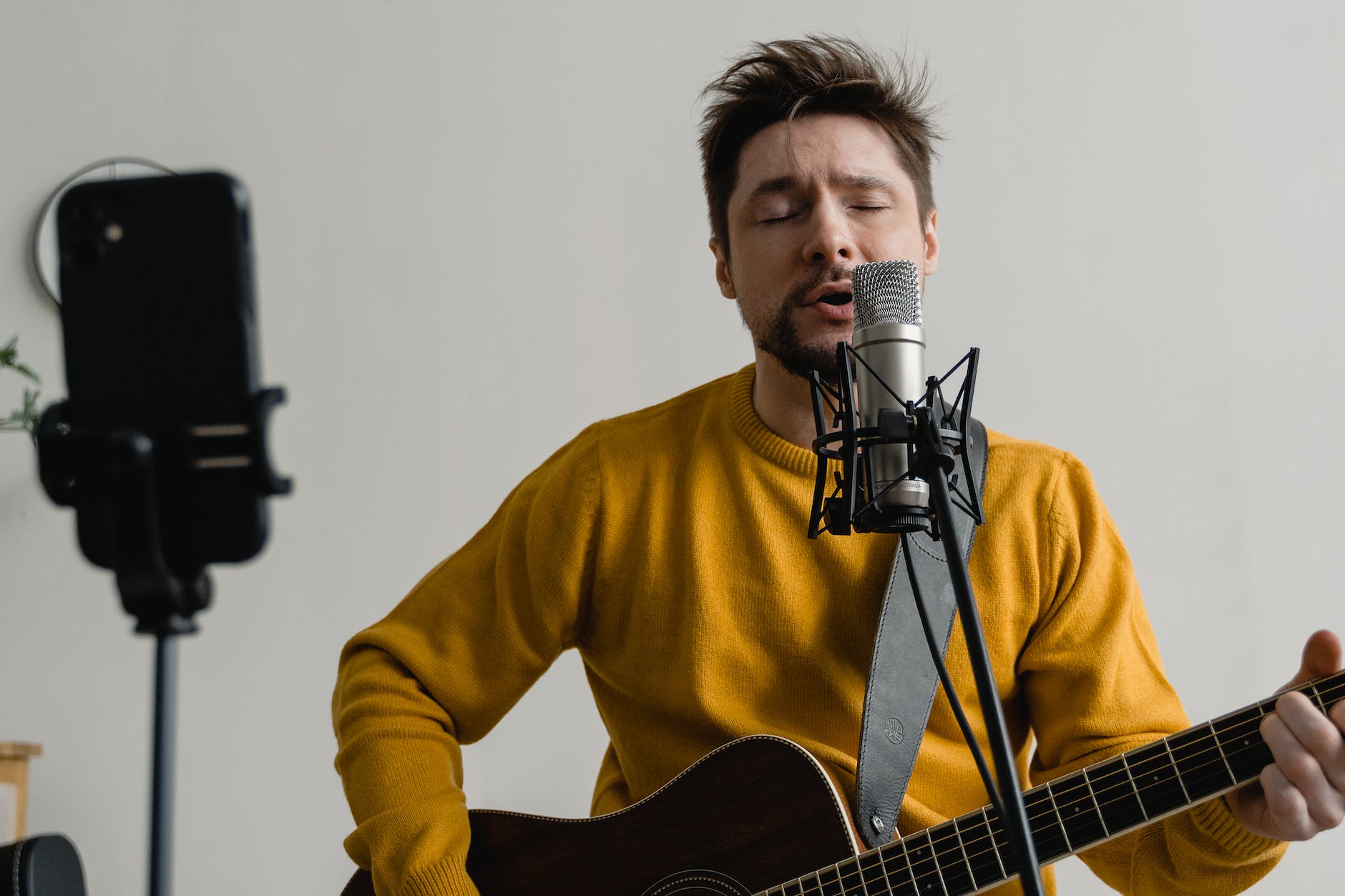 photo of a man in a yellow sweater singing while his eyes are closed