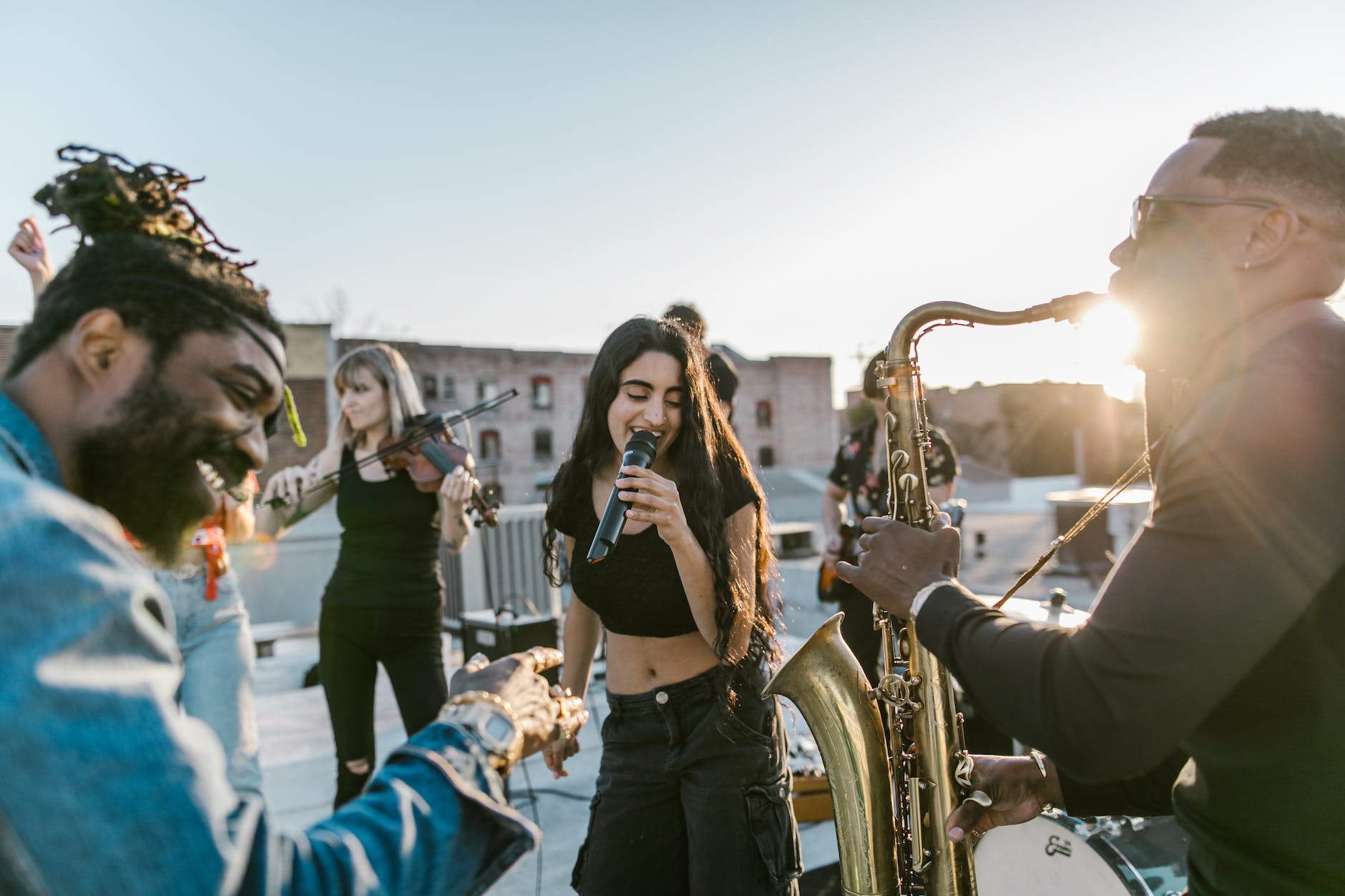 woman in black top singing beside man playing saxophone on the rooftop during golden hour